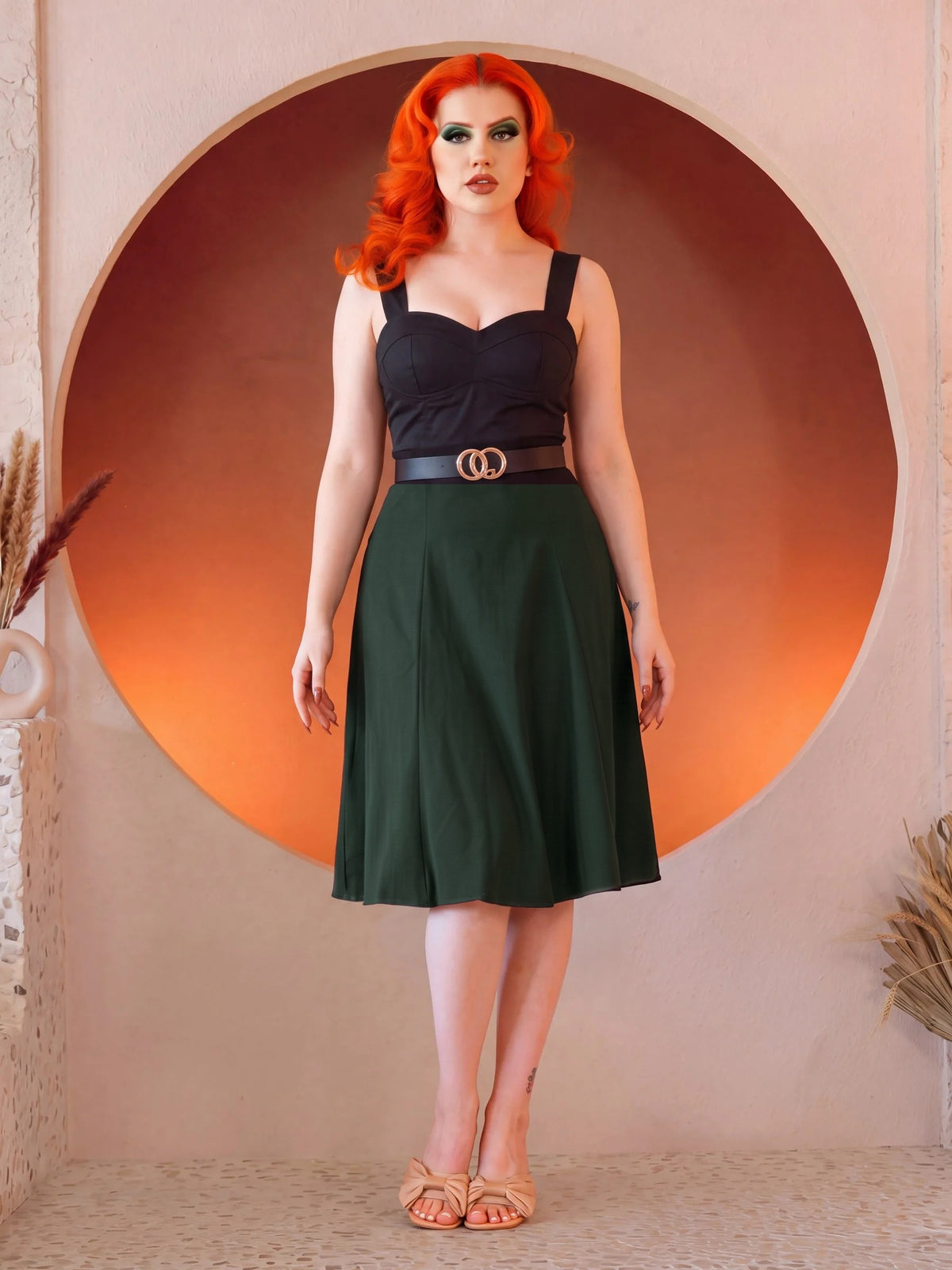 Front view of the Viva 40s Tulip Skirt in Hunter Green with the black Varla Top, the paneled skirt flaring from a belted waist to just below the knee, worn with tan bow sandals