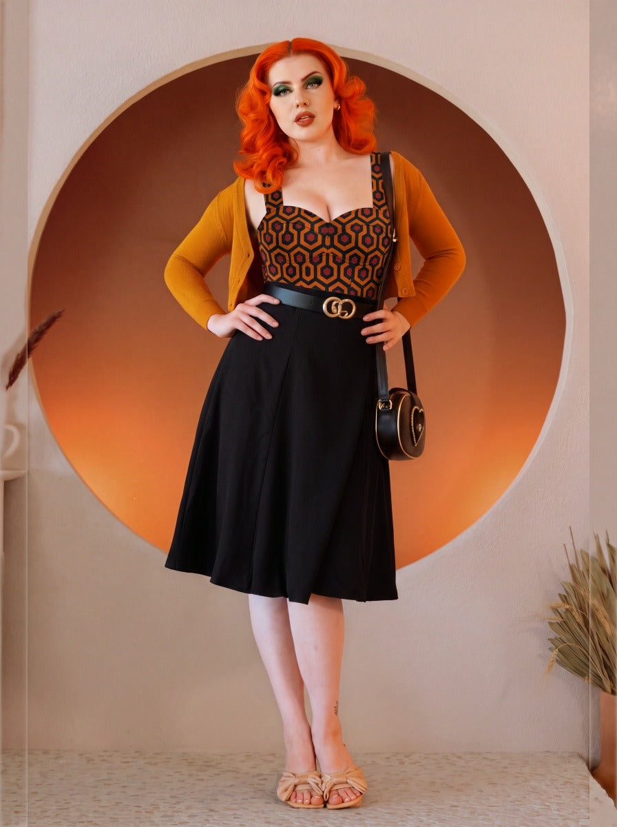 Model in the Varla Top in Hotel Hexagon, the orange and black hexagon bullet top with a sweetheart neckline, styled with the black Viva Tulip Skirt and a mustard cardigan