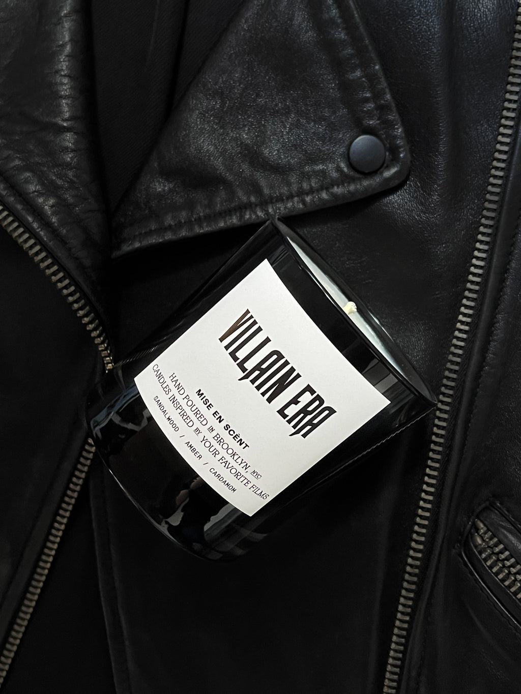 Villain Era candle in a black glass jar resting on a black leather jacket