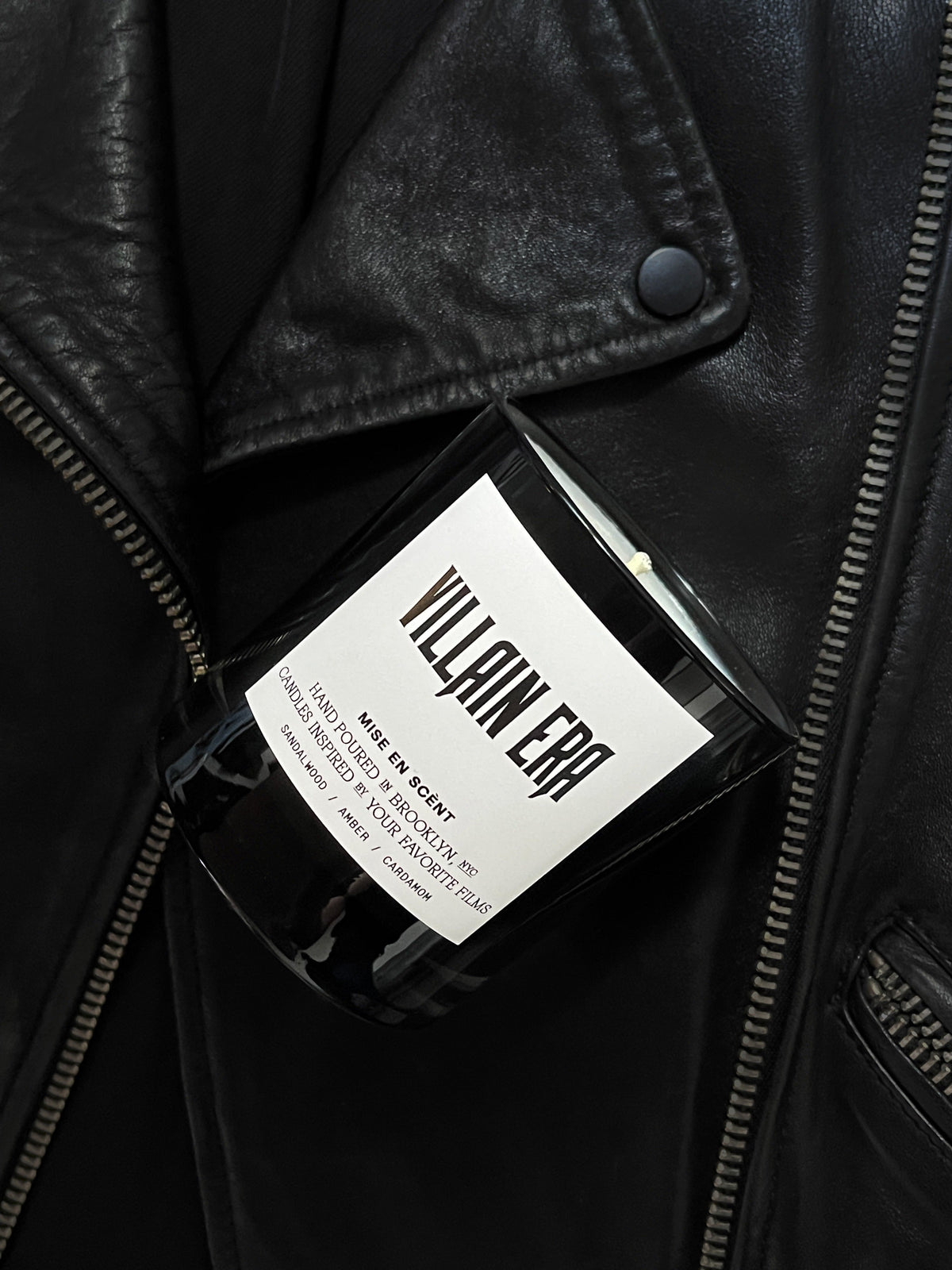 Villain Era candle in a black glass jar resting on a black leather jacket