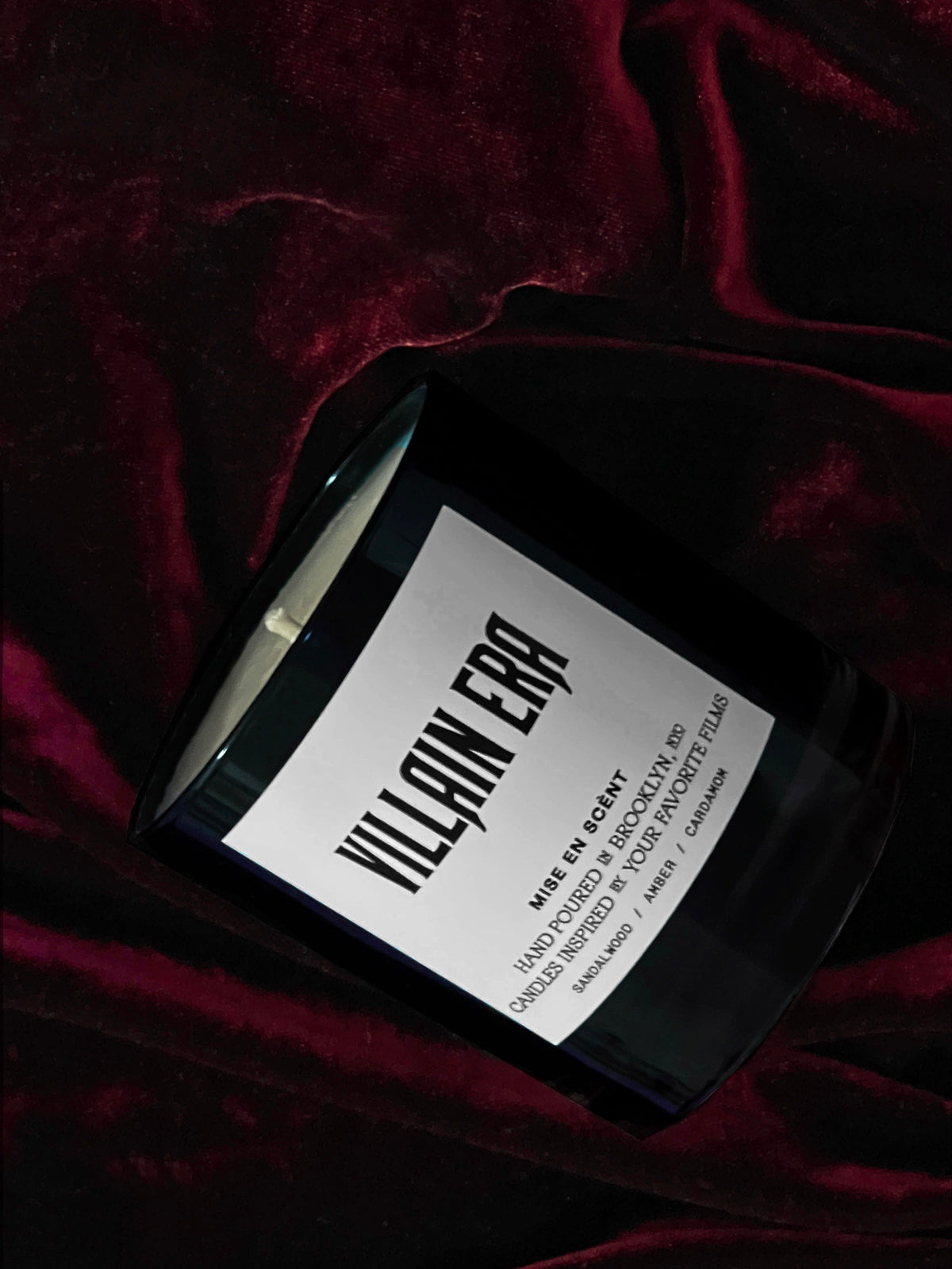 Villain Era candle lying on deep red velvet