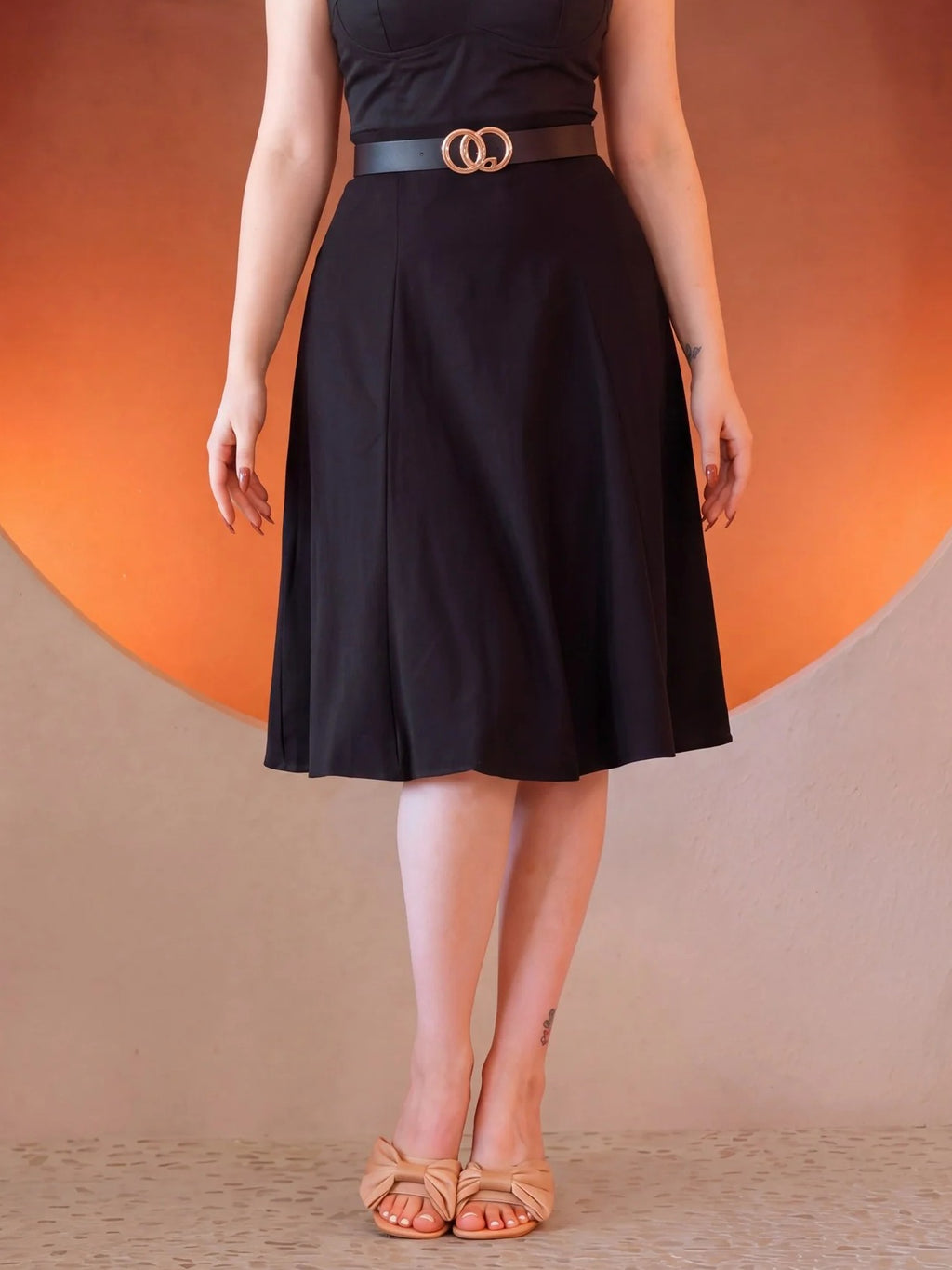 Front view of the Viva 40s Tulip Skirt in Black, high waisted with a gold ring belt, paneled skirt flaring to just below the knee, worn with tan bow sandals
