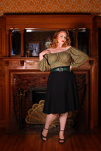 Model wearing the Viva 40s tulip swing skirt in black with a green and gold peasant top and a green snake buckle belt, front view