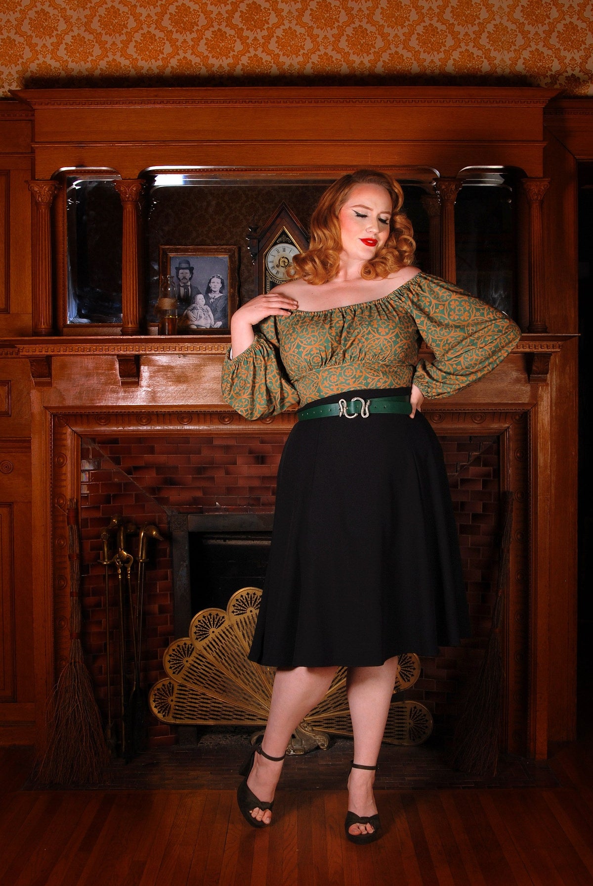 Model wearing the Viva 40s tulip swing skirt in black with a green and gold peasant top and a green snake buckle belt, front view