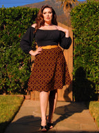 Model in the Viva 40s tulip skirt in orange and black Hotel Hexagon print, worn with a black peasant top and a mustard belt