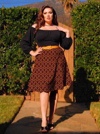 Model in the Viva 40s tulip skirt in orange and black Hotel Hexagon print, worn with a black peasant top and a mustard belt
