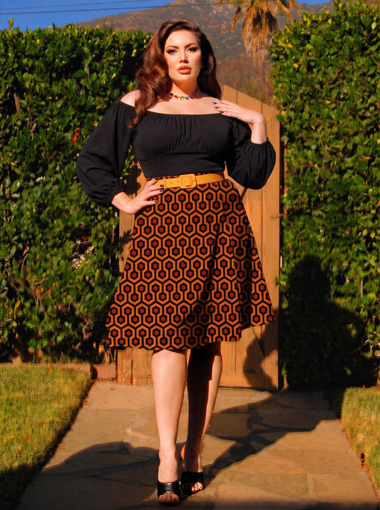 Model in the Viva 40s tulip skirt in orange and black Hotel Hexagon print, worn with a black peasant top and a mustard belt