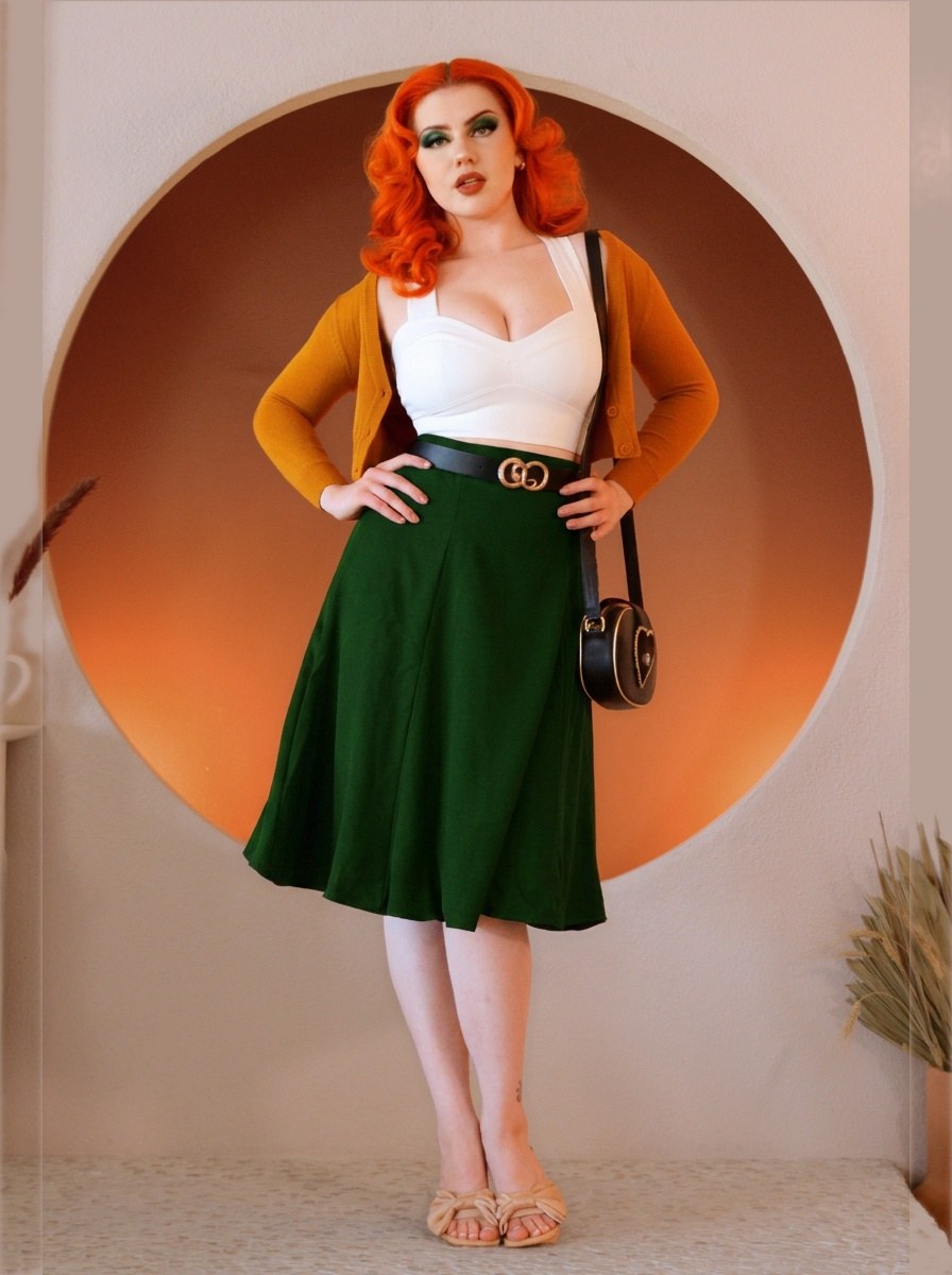 Model wearing the Viva 40s tulip swing skirt in hunter green with a white crop top, mustard cardigan and black belt