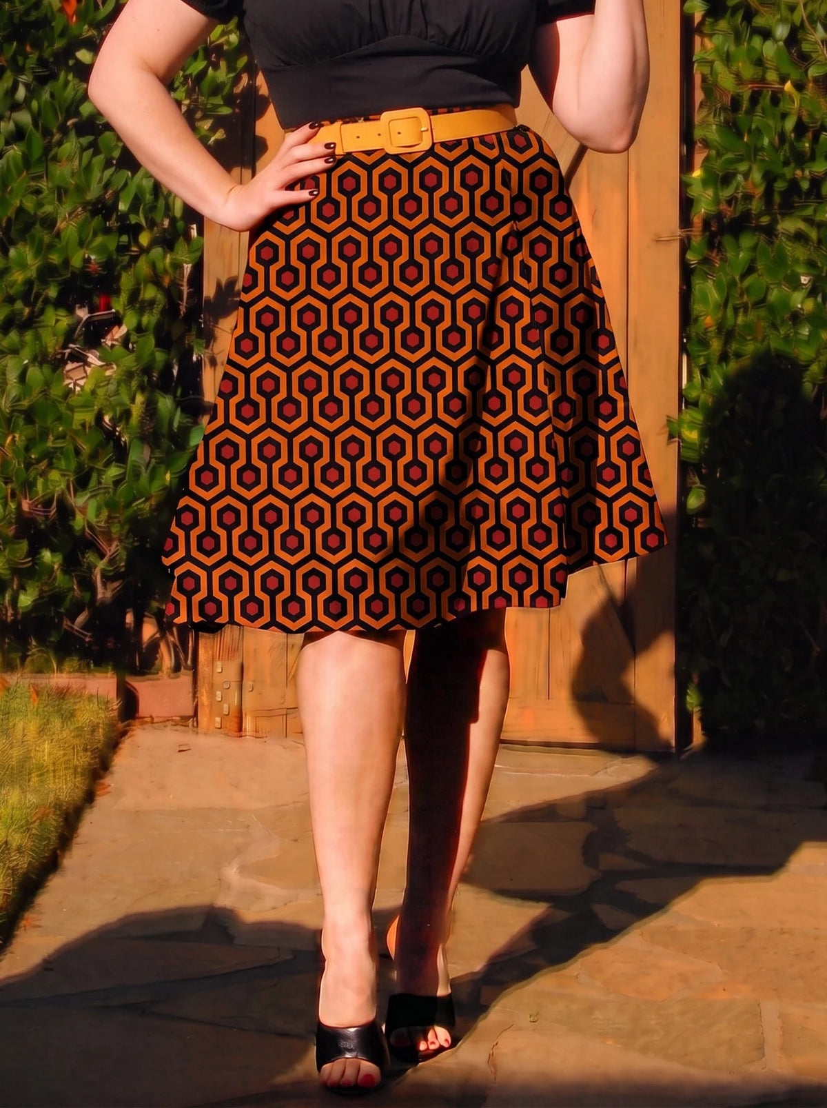 Waist-down view of the Viva 40s tulip skirt in the Hotel Hexagon print with a mustard belt and black peep toe mules