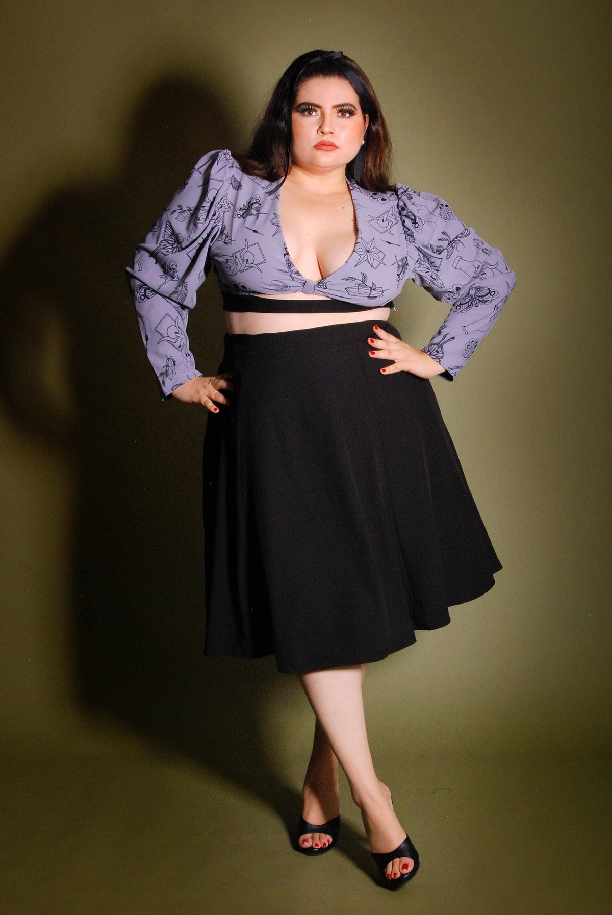 Model wearing the Viva 40s tulip swing skirt in solid black with a lilac blouse, showing the high waist and flared knee-length skirt