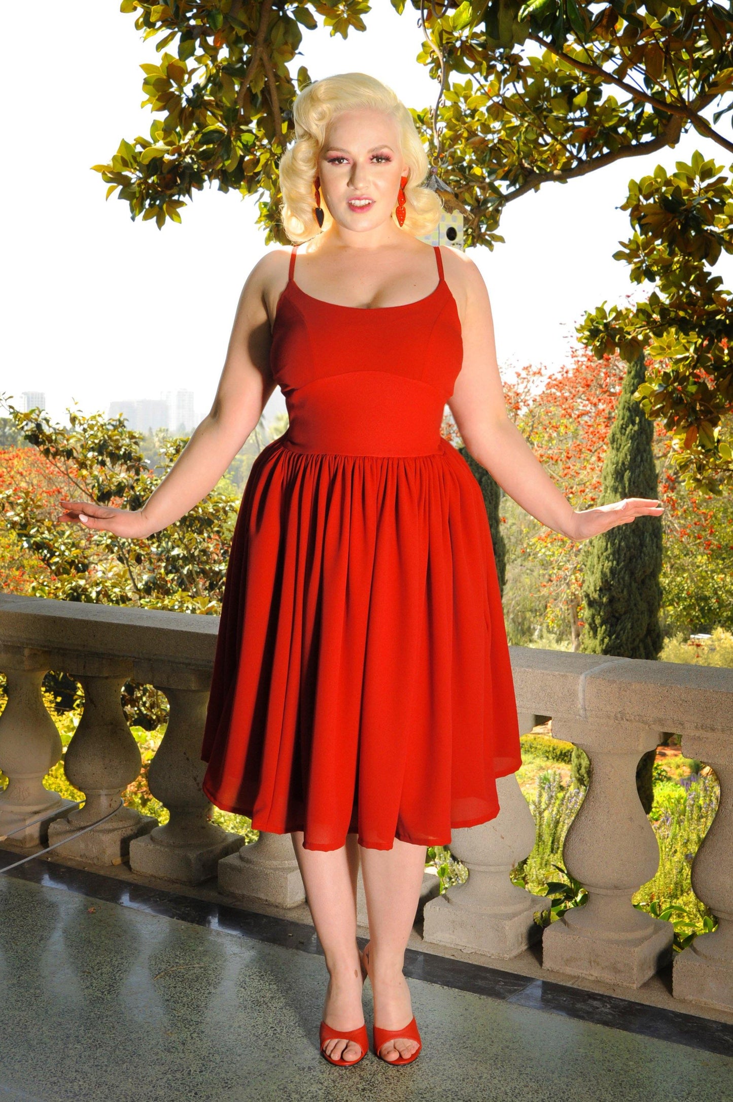 Pictured is Pinup Girl Clothing model Nicole Amelia in the PUG staple 1960’s style Jenny sundress in cherry red crepe with full, gathered skirt and deep pockets, finished with a long back zip, adjustable straps and sculpting seam under the chest for a large range of bust sizes and no bodice boning.